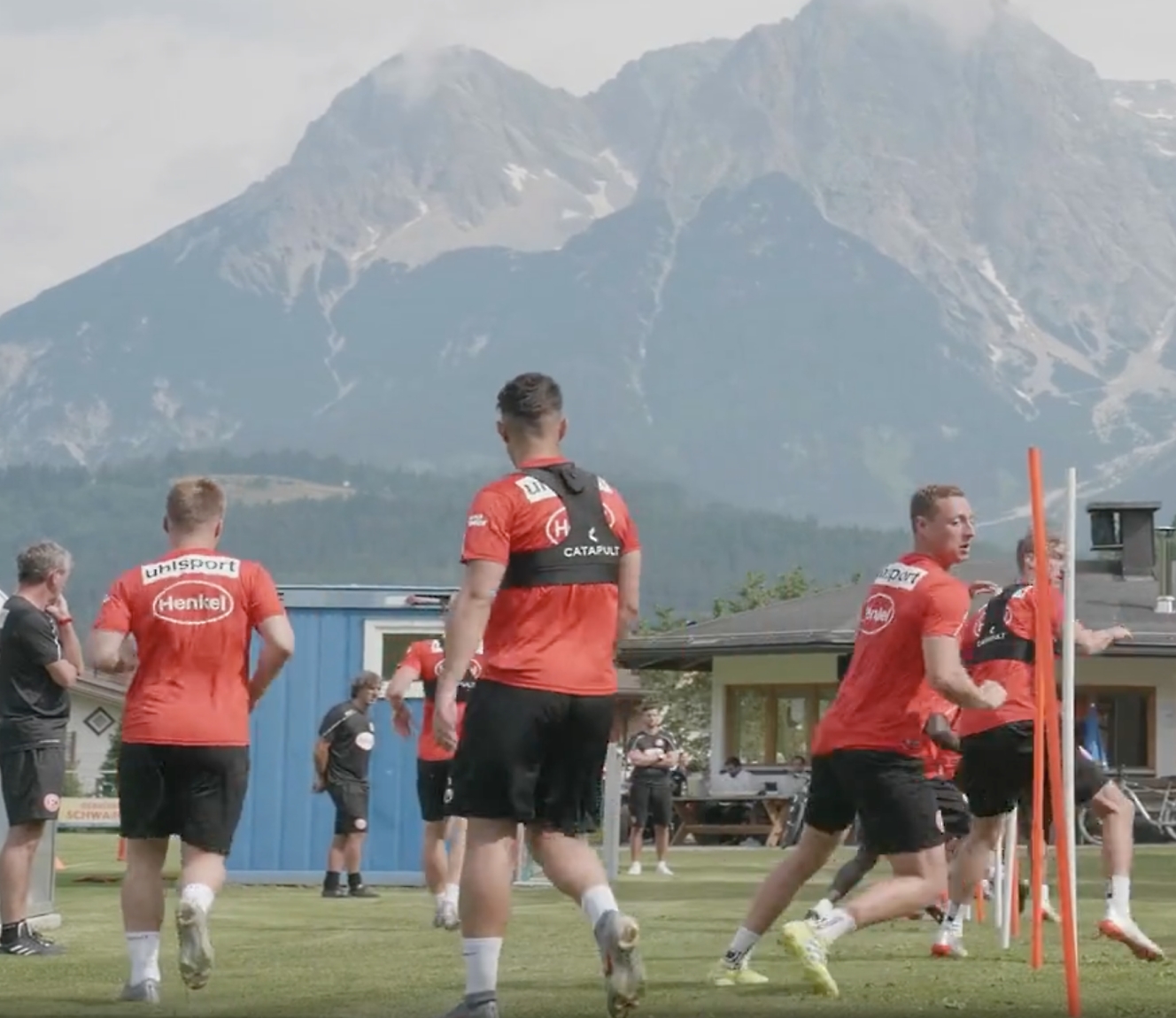 Fußballspieler in roten Trikots, die im Freien mit einem Blick auf die Berge im Hintergrund trainieren.