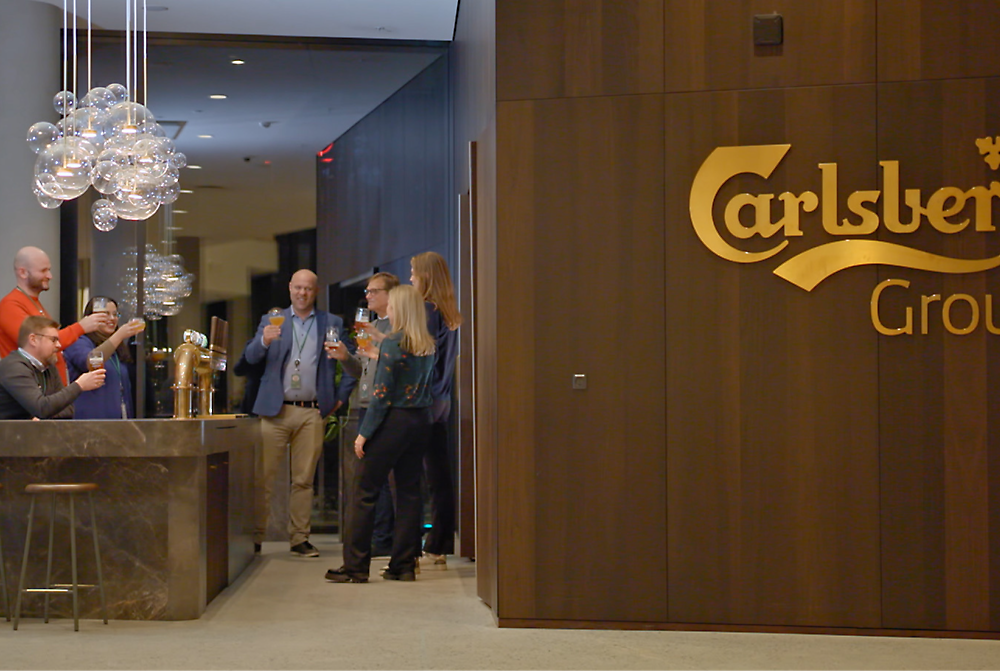 People conversing near the entrance of the carlsberg club, with one man serving drinks.