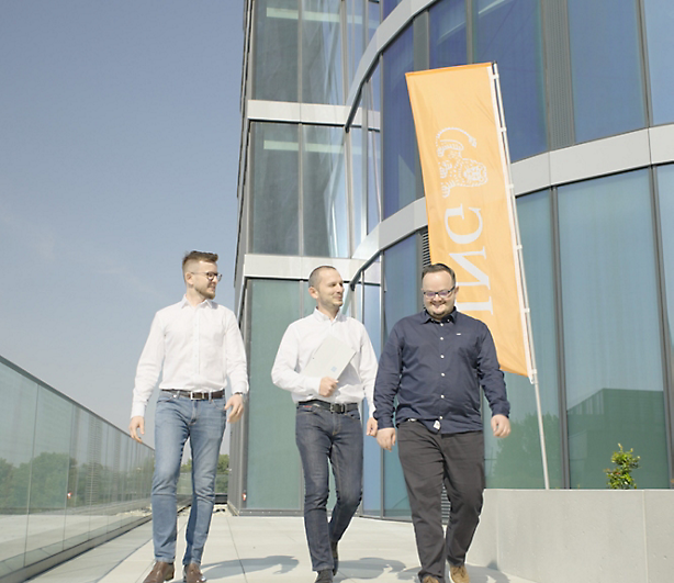 Trois hommes qui marchent devant un bâtiment avec une bannière de logo ING dessus.