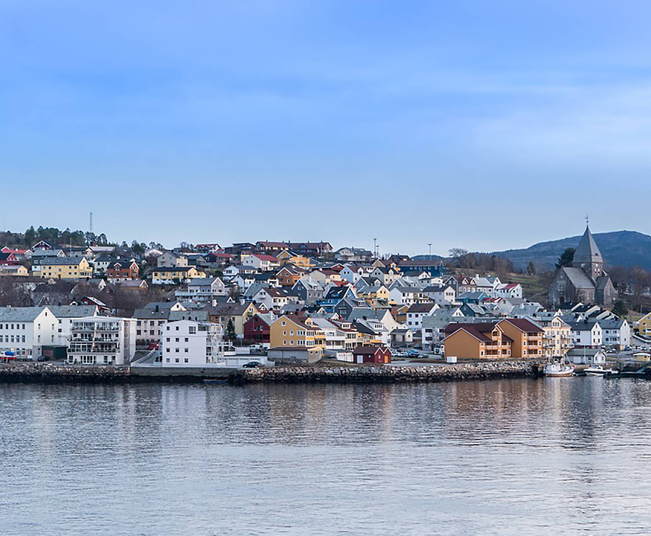 Coastal town with colorful houses by the water under a cloudy sky.