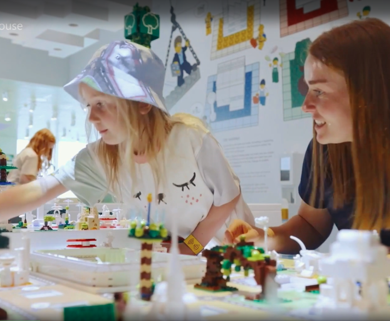 Deux femmes qui interagissent avec un modèle de Lego dans une exposition interactive, l’une portant une protection faciale.