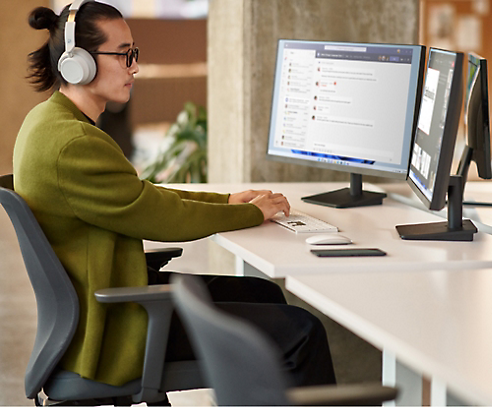 En person er iført hovedtelefoner og sidder ved et skrivebord med to computerskærme