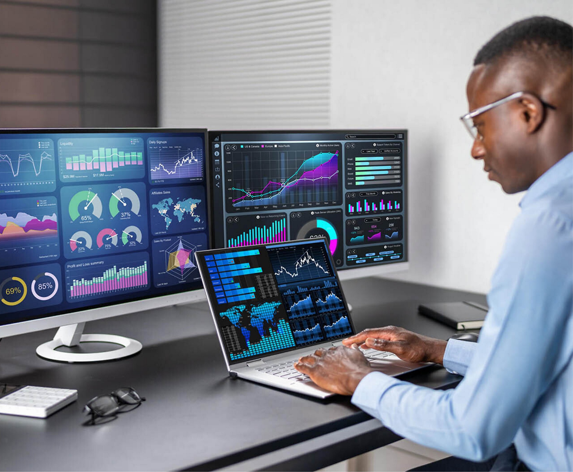 A man analyzes financial data on multiple computer screens in a modern office setting.