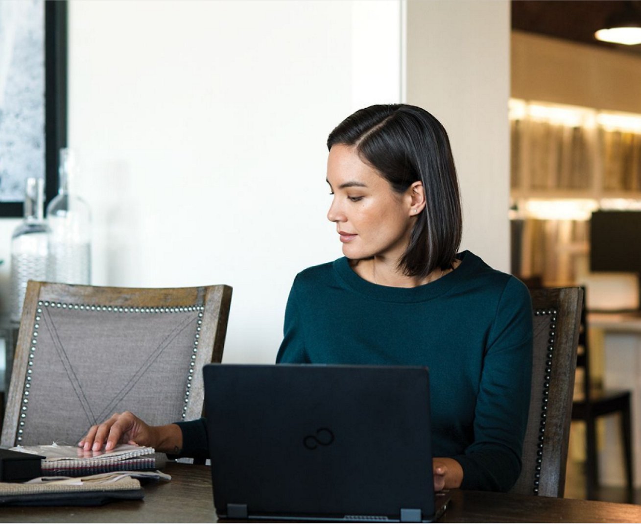 Kobieta pracująca na laptopie, a także notesy umieszczone na jej biurku