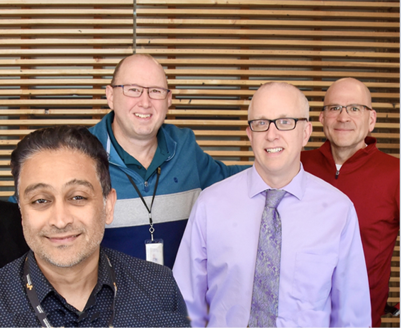 Four men posing for a photo in front of a wooden wall.