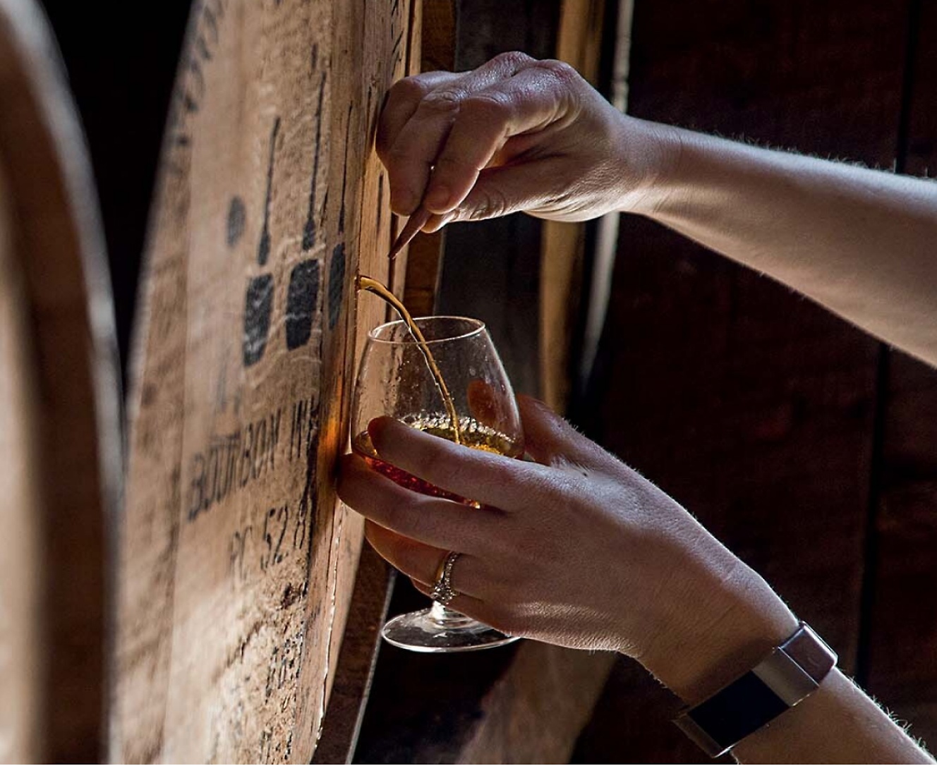 Una persona sirviéndose un vaso de whisky de un barril.