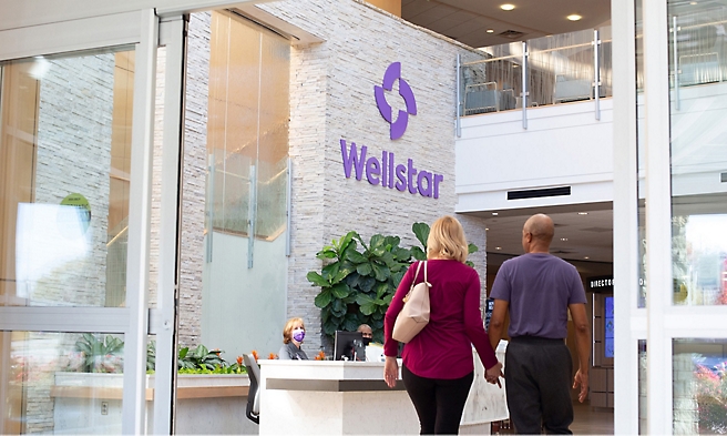 Two people walking in front of a wellstar building.