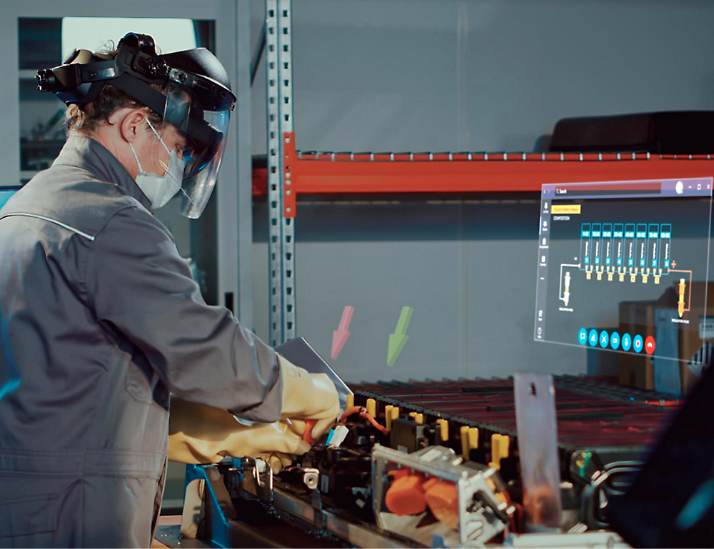 Technician wearing protective gear and a face mask works on machinery while monitoring data on a screen in an industrial setting.