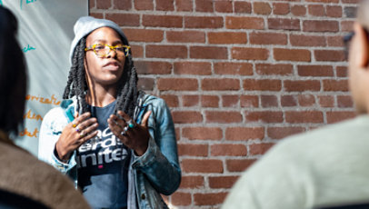 A woman delivers a speech in front of an audience.