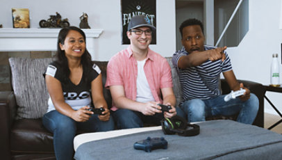 Three people joyfully play with an Xbox in a living room.