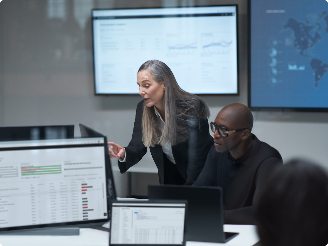 Two persons are watching computer and one person pointing at a computer screen