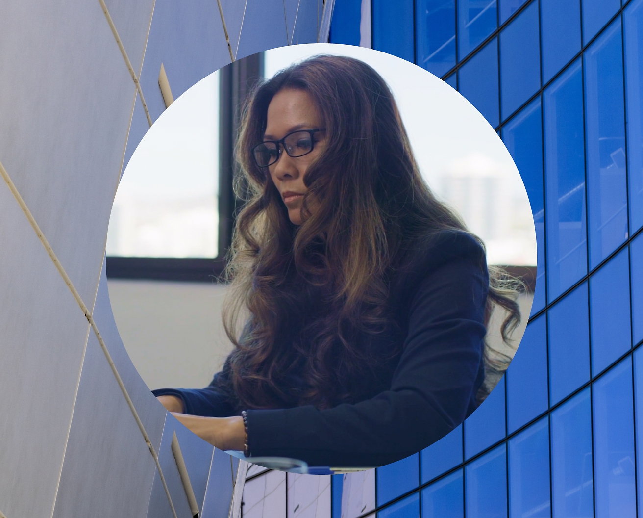 אישה עובדת על המחשב הנישא שלה מרכיבה משקפיים ותמונת רקע מוגדרת כבניין מזכוכית