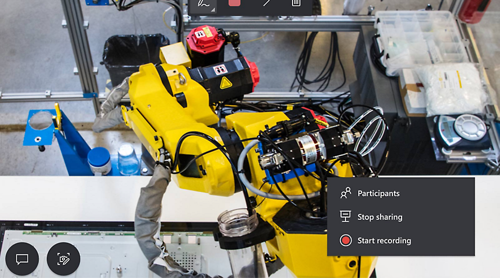 View of a robotic arm in a workspace, with video conferencing controls visible on the screen