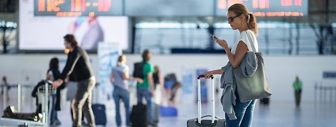 Jovem com sua bagagem em um aeroporto internacional, antes de passar pelo check-in e pela verificação de segurança antes do voo.