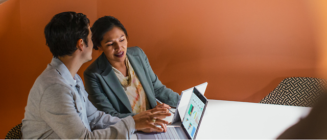 Two professionals collaborating on a project using a laptop in a warmly lit office space.