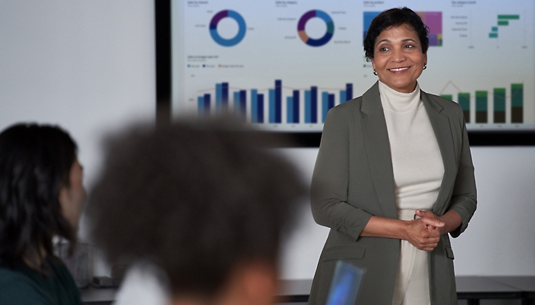 En kvinne i en forretningsdress som står foran en skjerm med grafer på den.