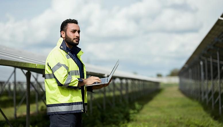 En mann med en bærbar datamaskin foran solpaneler.