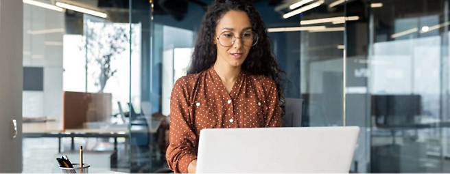 Eine Person in einem braunen Hemd und einer Brille, die an einem Computer arbeitet