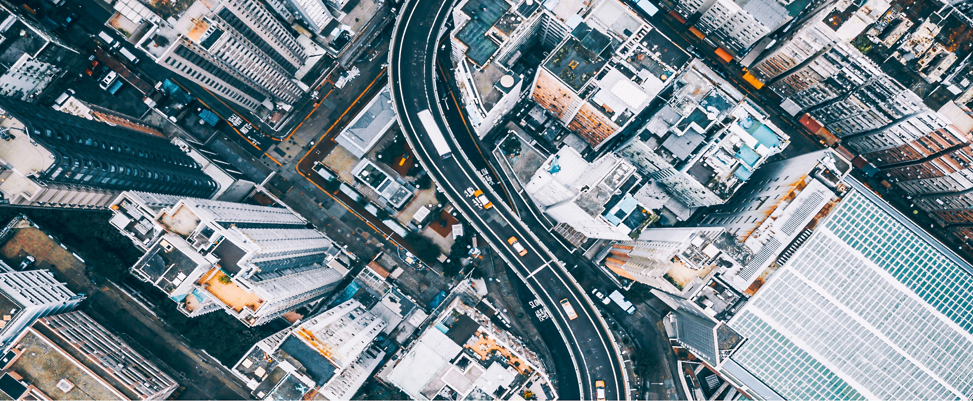 Aerial view of a bustling city with dense buildings intersected by curving roads, covered in snow.