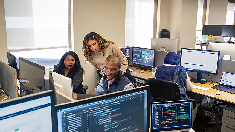 Tres personas en una oficina mirando la pantalla de una computadora.