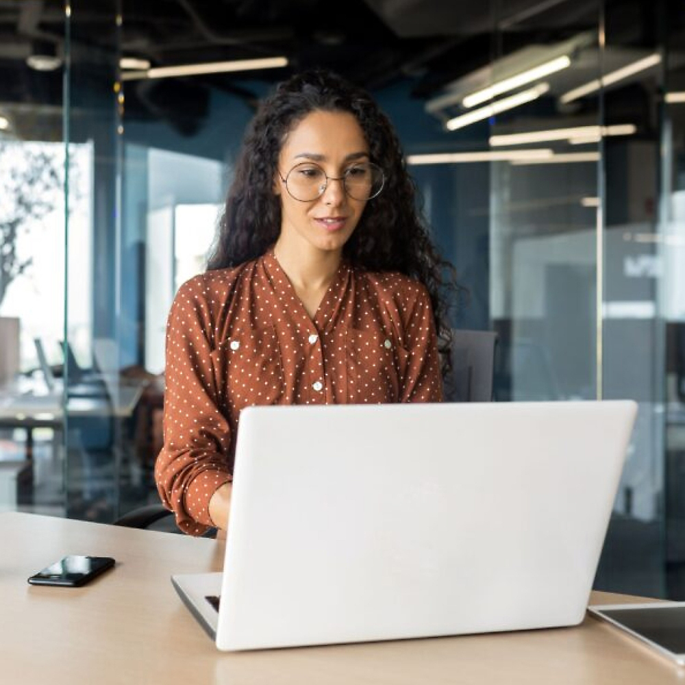 Uma pessoa sentada à mesa com um computador e usando óculos.