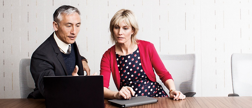 Um homem e uma mulher sentados em uma mesa, olhando para uma tela de laptop e discutindo algo