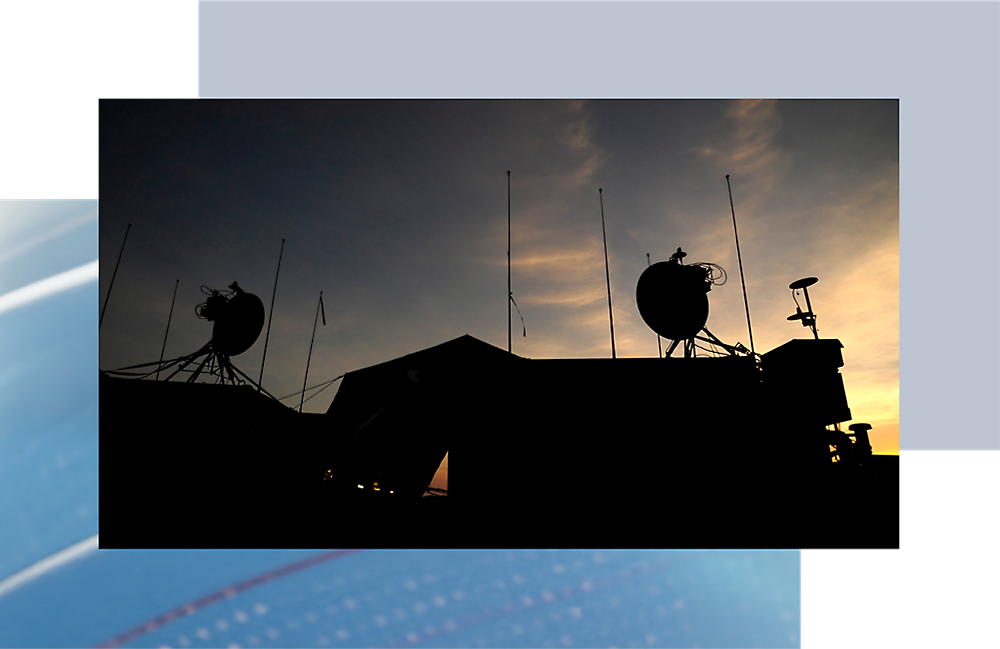 Silhouet van communicatieantennes op een dak tegen een zonsondergang met levendige oranje en blauwe tinten.