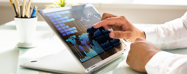 Person som analyserer økonomiske data på en nettbrettskjerm med interaktive diagrammer og grafer i en lys kontorsetting.