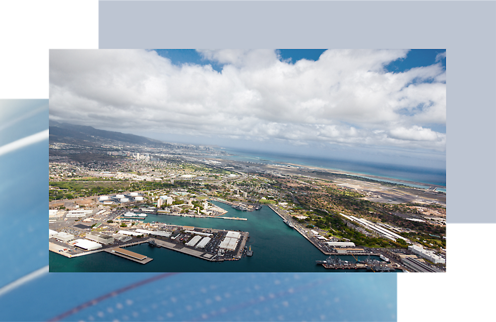 Aerial view of a coastal city with an industrial harbor and a dense urban skyline under a partly cloudy sky.