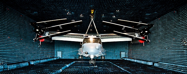 A helicopter undergoing testing inside an anechoic chamber covered with blue foam pyramidal sound absorbers.