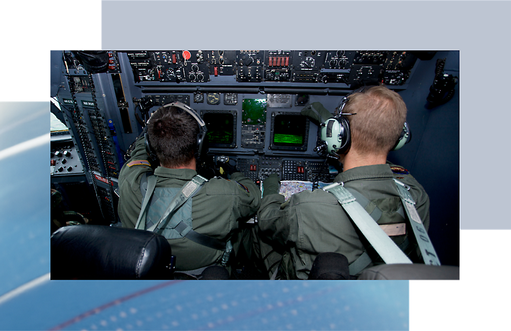 Twee piloten die besturingselementen bedienen in de cockpit van een vliegtuig, van achteren bekeken, met focus op het instrumentpaneel.