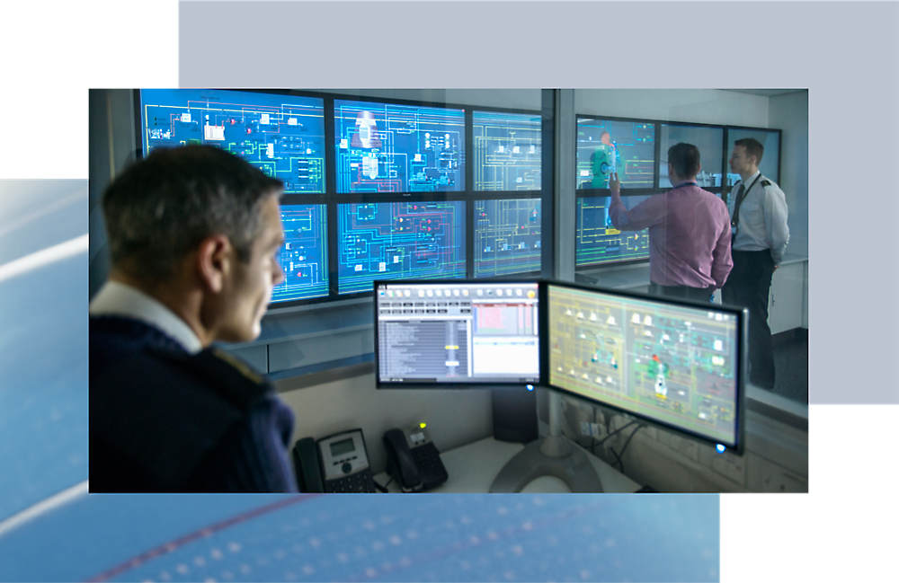 Three people in a control room with multiple screens displaying various data and maps, one person actively pointing at a screen.