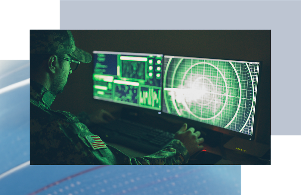 Een militair in een camouflage uniform analyseert gegevens op een computer met meerdere schermen waarop radar- en digitale kaarten worden weergegeven.