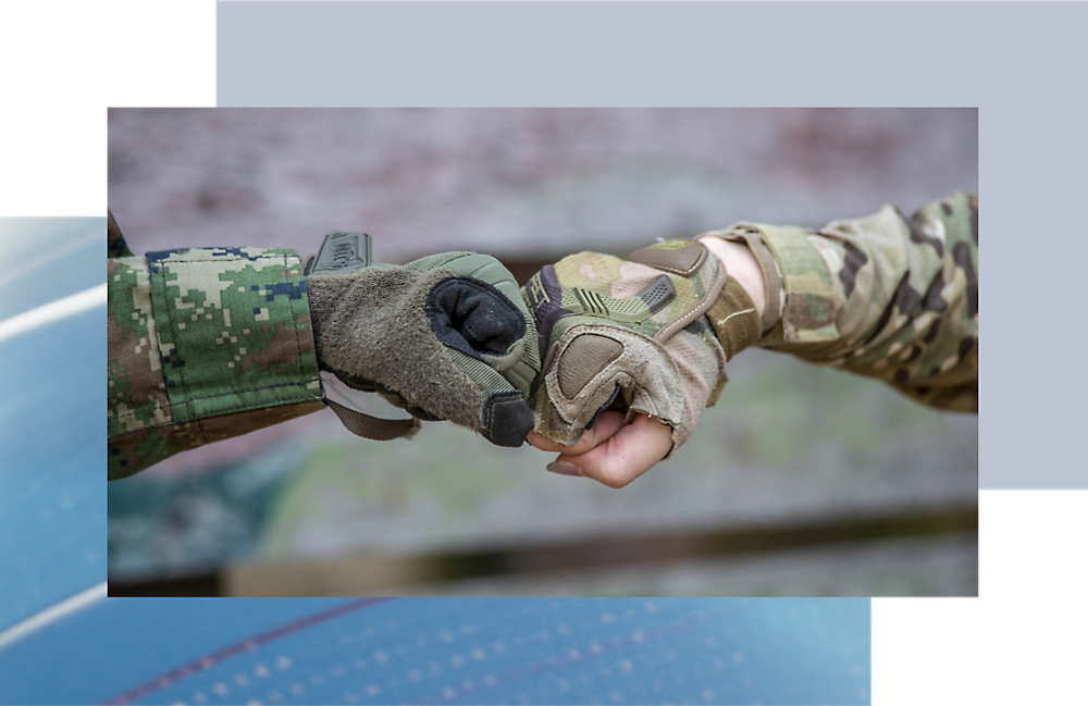 Dos personas con uniforme militar chocan los puños, centrándose en sus manos enguantadas.