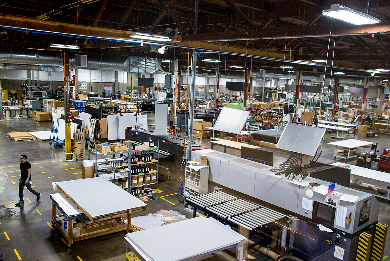 A large, well-lit manufacturing facility with various workstations, machinery, and materials. 