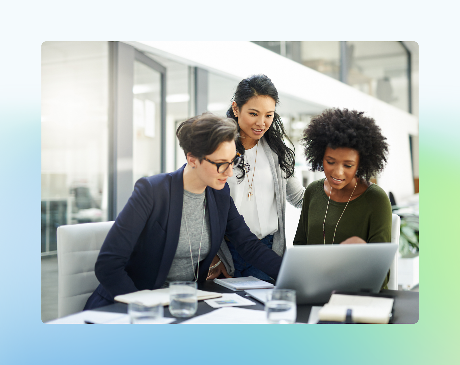 Tres mujeres diversas colaborando frente a un portátil en un entorno de oficina moderno.