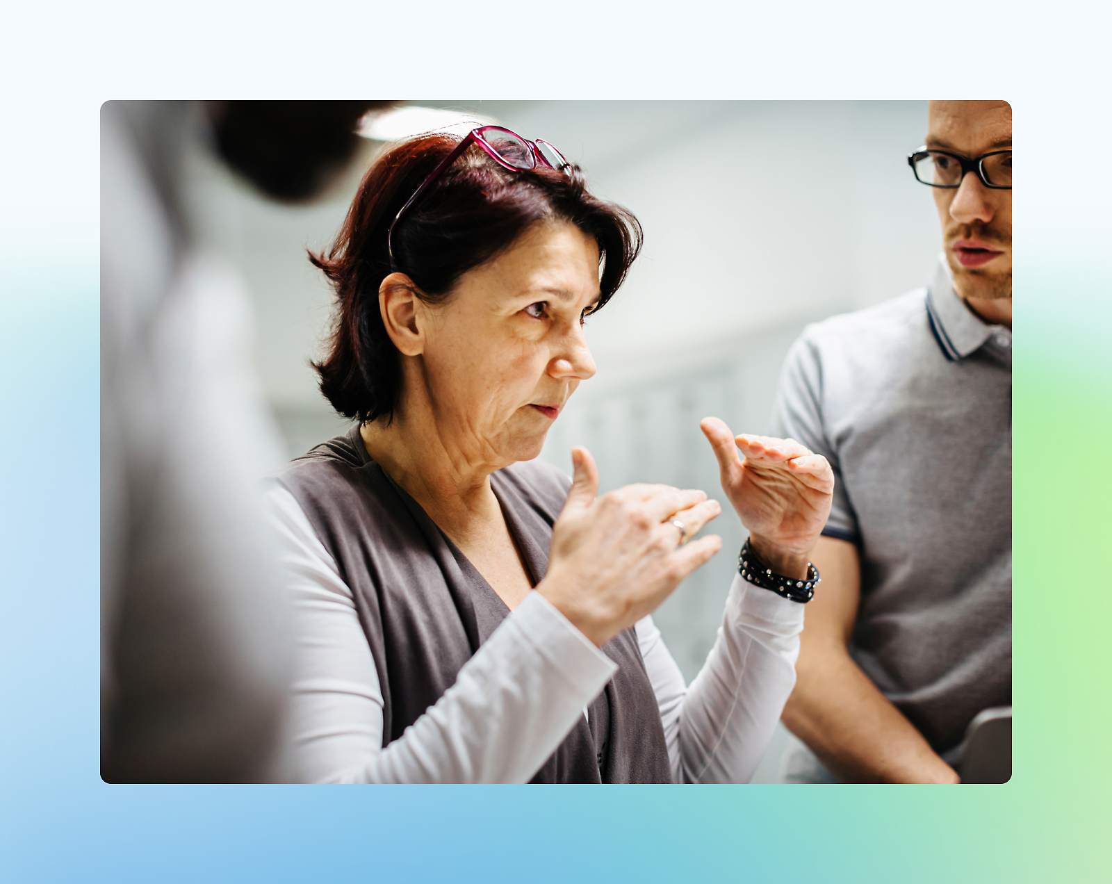 Three professionals in a discussion, with an older woman gesturing expressively to two younger male colleagues