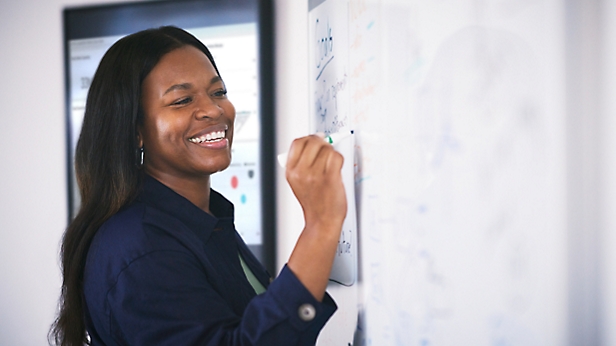 Femme souriante écrivant sur un tableau blanc dans un bureau.