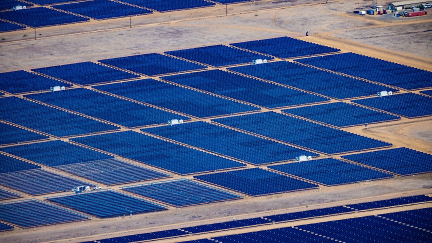 Vue aérienne d'une grande ferme solaire avec des rangées de panneaux solaires bleus soigneusement disposés dans un paysage aride.