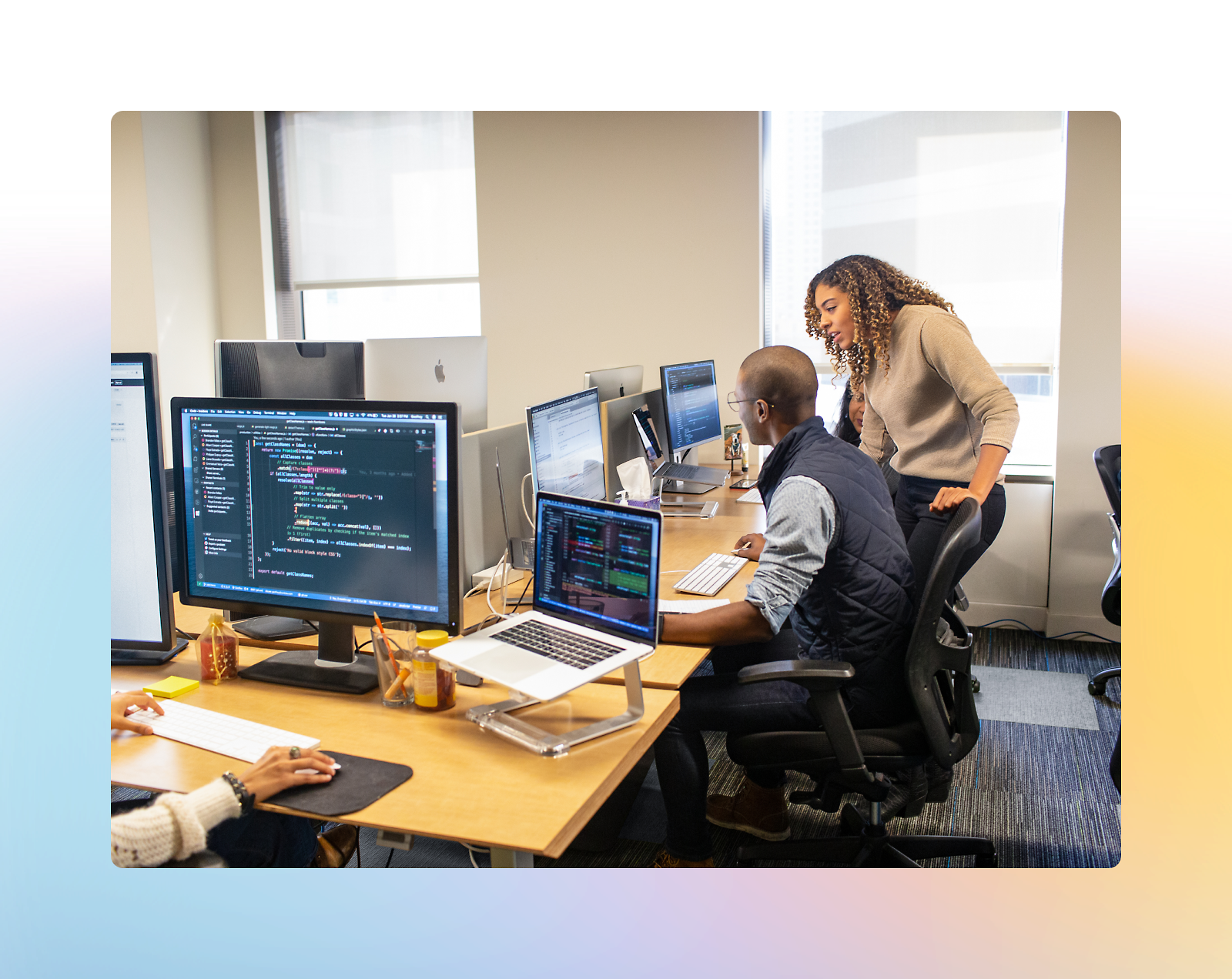 Three people work at desks with multiple computer monitors displaying code in an office setting. 