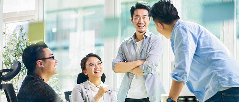 Four people are engaged in a discussion in a bright office space. Three are standing, and one is seated