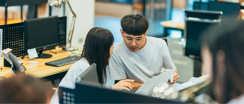 Two people in an office setting are closely discussing something on a laptop screen