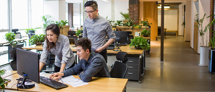 Three colleagues collaborating on a project, looking at a computer screen in a modern office with plants 