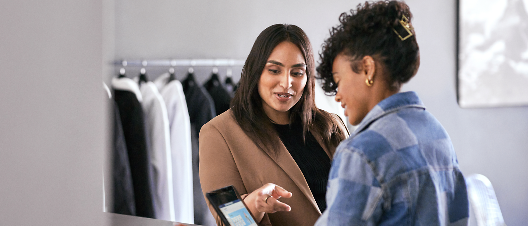 Two women discussing over a digital tablet in a clothing store, one is showing something on the screen to the other.