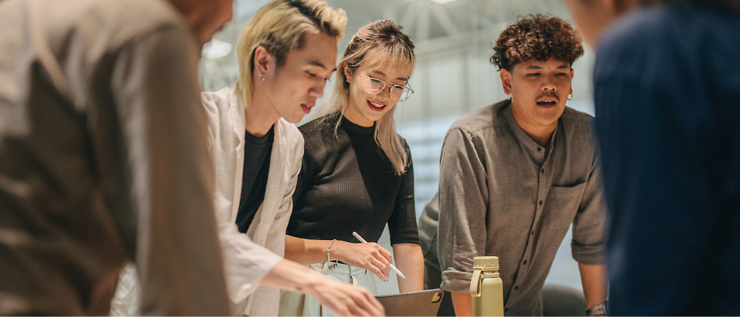 Three young adults, two men and one woman, engaged in a discussion over a document at a well-lit workspace.