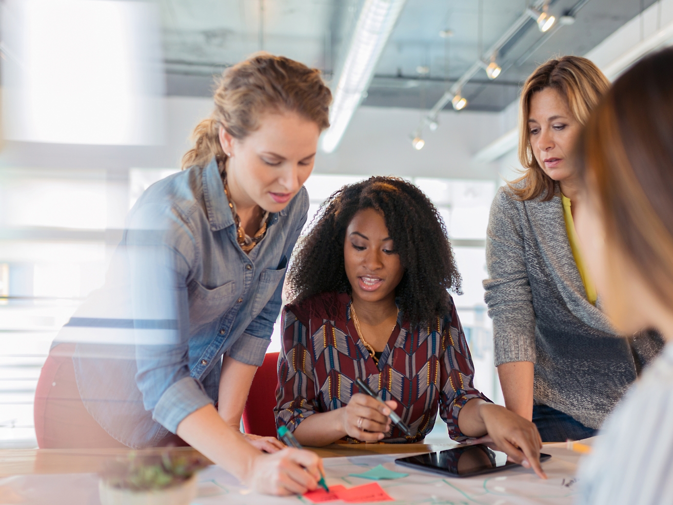 Vier Frauen, die an einem Tisch in einem hell beleuchteten Büro zusammen an Dokumenten arbeiten.