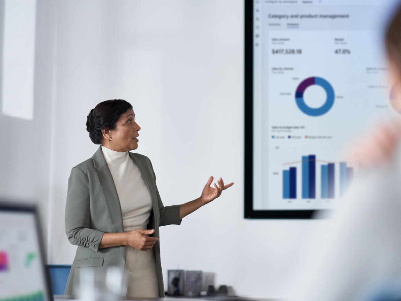 En kvinna presenterar ekonomiska data på en skärm för sin publik i en modern kontorsmiljö.