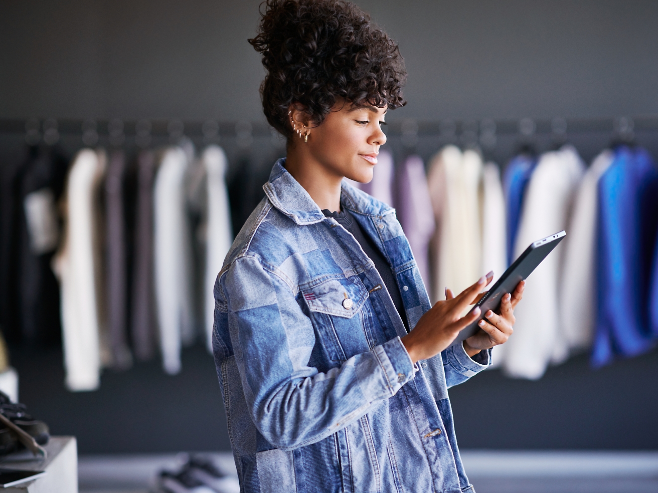 A woman in a denim jacket is using a tablet in a clothing store