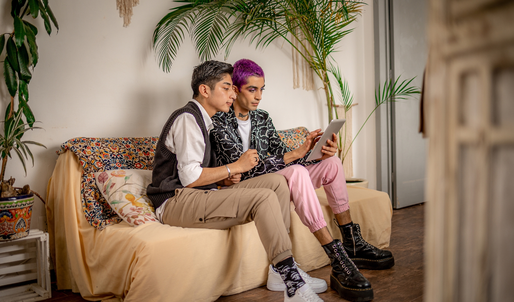 Dos personas sentadas en un sofá mirando una tableta. Una tiene el pelo gris corto y lleva pantalones beige