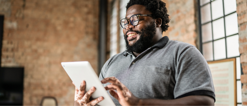 A cheerful bearded man using a tablet in a loft workspace.